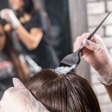 Close up of female hairdresser's hands are dyeing client's hair in front of the mirror in beauty salon
